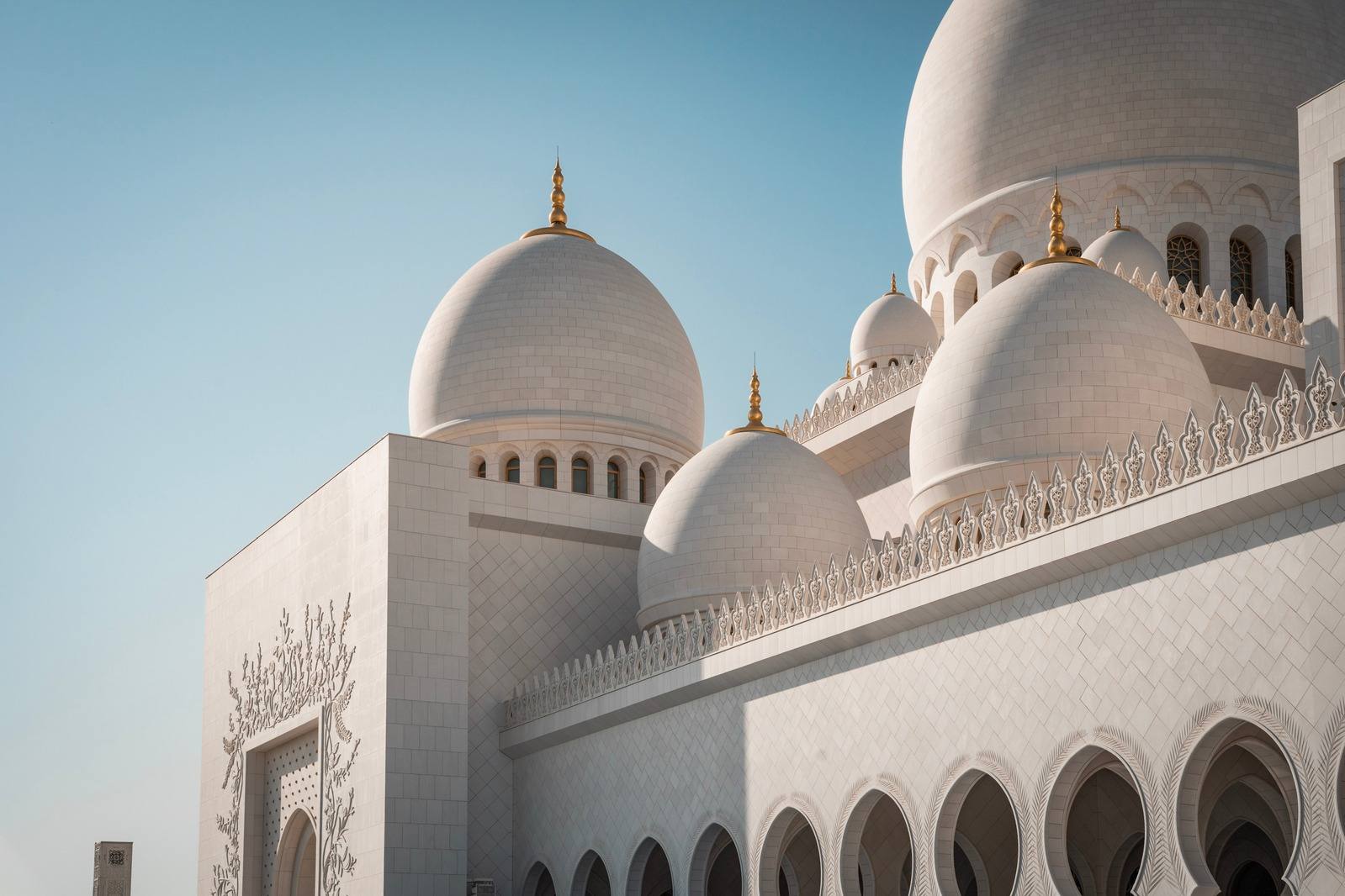 White domes of Sheikh Zayed Grand Mosque against a clear sky